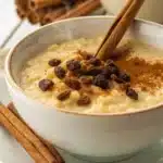 Arroz con leche garnished with a cinnamon stick and raisins in an ornate bowl.