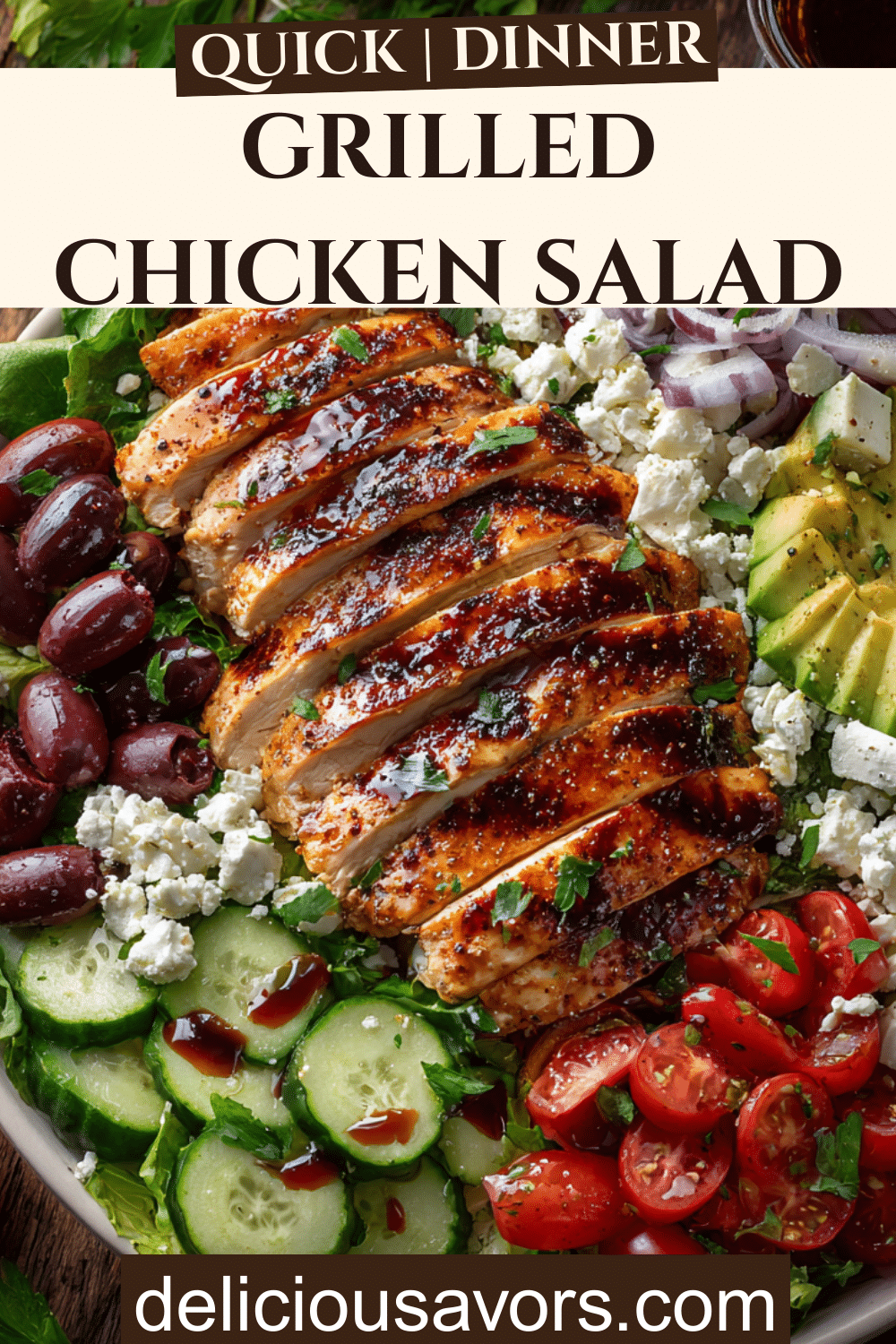 Overhead view of grilled chicken salad in white bowl with charred chicken slices, romaine lettuce, cherry tomatoes, cucumbers, avocado, Kalamata olives, and crumbled feta cheese drizzled with red wine vinaigrette